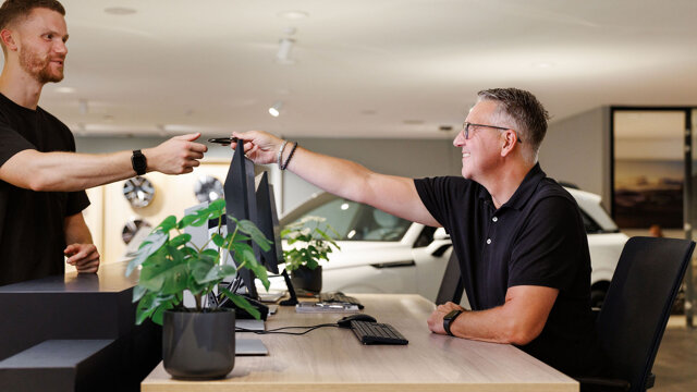 Medewerker overhandigt autosleutel aan klant bij een bureau in de showroom