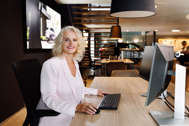 Medewerker in lichte blazer werkt achter een computer aan een bureau in de showroom