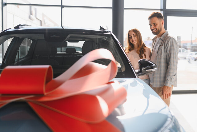 Een man en vrouw bekijken een auto met een grote rode strik op de motorkap in de showroom