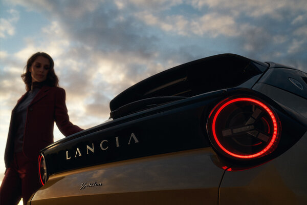 Achterkant Ypsilon met vrouw en lucht Vrouw leunt op de achterkant van de Lancia Ypsilon Electric